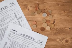 Flat lay of tax forms and scattered coins on a wooden table, illustrating finance and taxation concepts.
