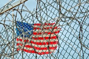 Australian deported: USA flag through barbed wire, symbolizing protection & freedom.